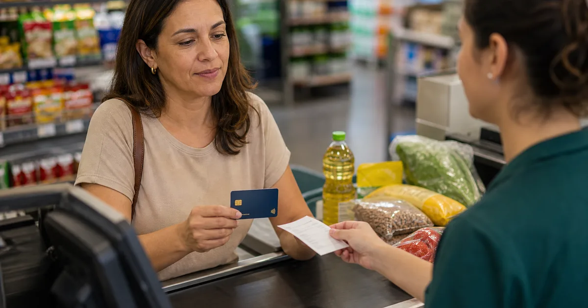 Cliente paga compras no mercado com cartão sem marca enquanto recebe recibo no caixa.